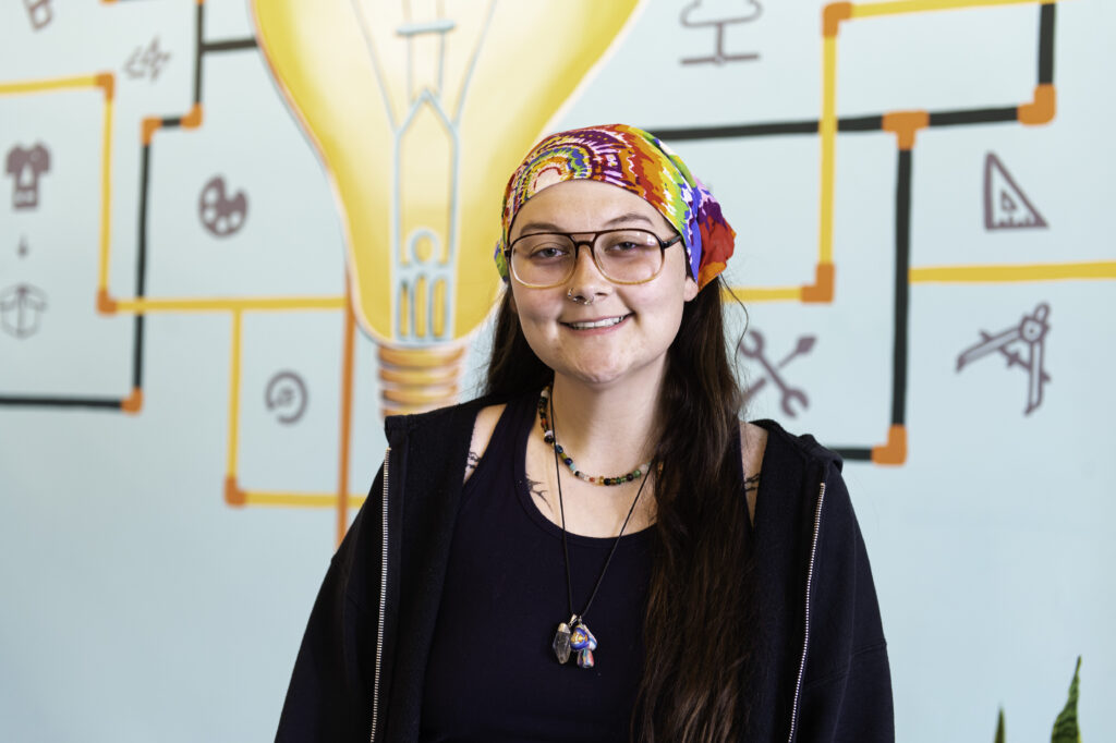 Carmen smiling at the camera with Spark on 7th's mural of a interconnected light bulb in the background.