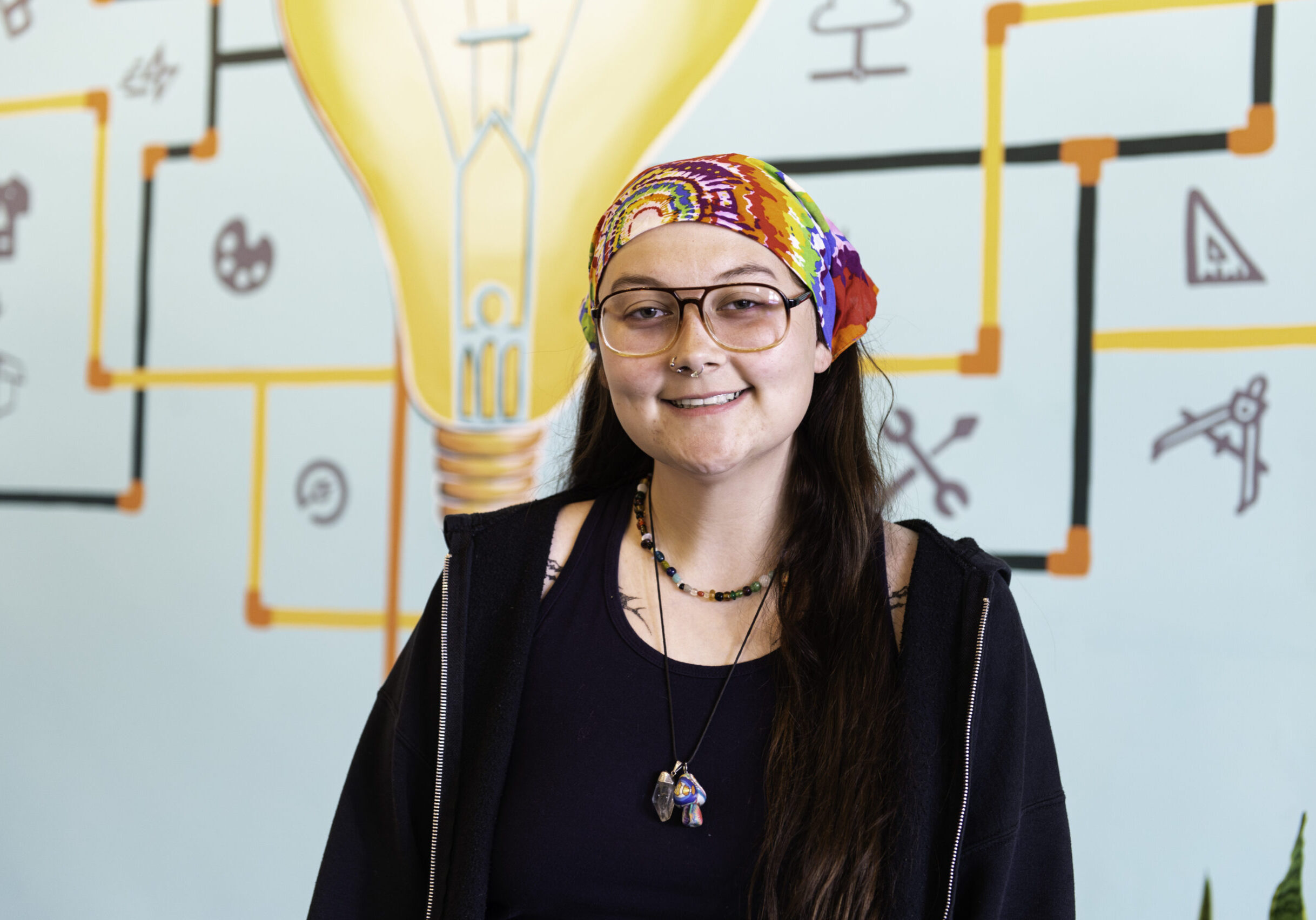 Carmen smiling at the camera with Spark on 7th's mural of a interconnected light bulb in the background.